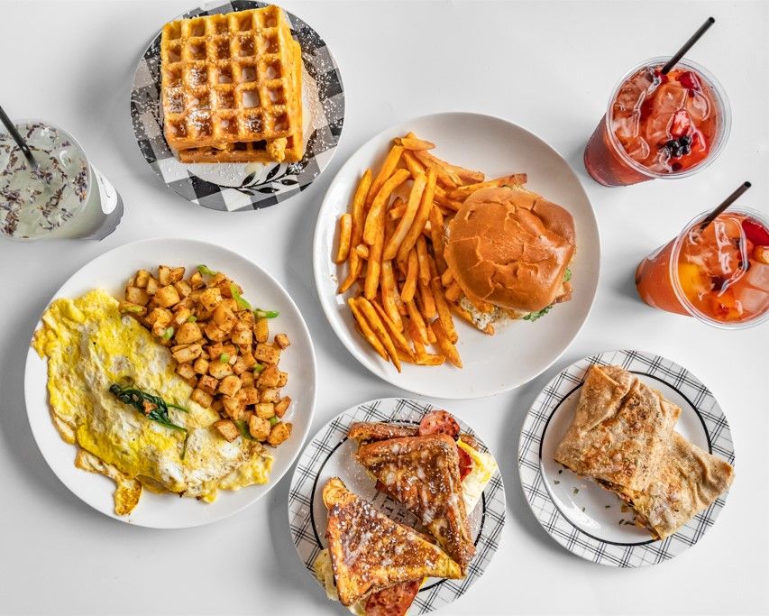 A spread of Haven Café dishes: waffles, an omelette with home fries, a loaded burger with fries, French toast sandwiches, a breakfast wrap, and iced drinks.
